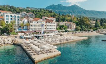 a picturesque beach scene with numerous lounge chairs and umbrellas set up on the sand , surrounded by a body of water at Hotel Perla