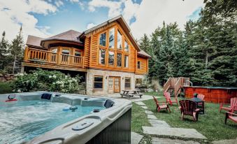 a large wooden house with a hot tub in the backyard , surrounded by trees and grass at Fiddler Lake Resort