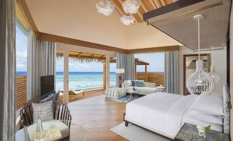 a luxurious hotel room with a large bed , a tv , and a view of the ocean at JW Marriott Maldives Resort & Spa