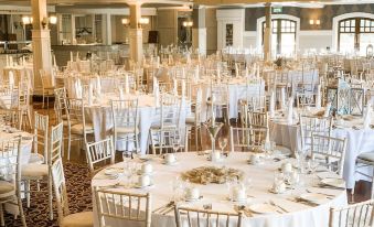 a large , ornate banquet hall with numerous round tables covered in white tablecloths and chairs arranged for a formal event at Mulroy Woods Hotel