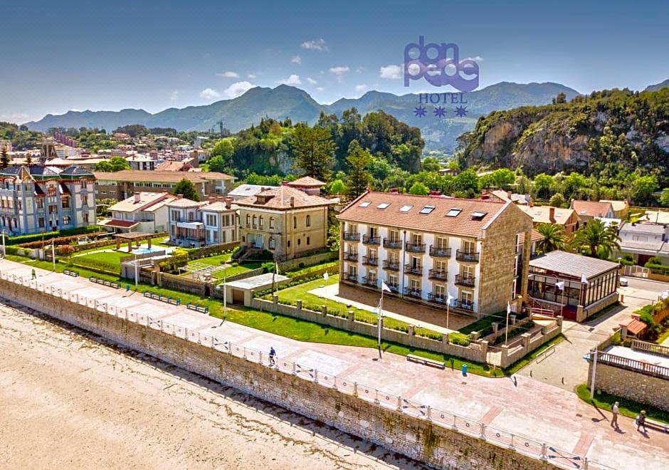 a large , white building with a sign on the side is surrounded by green grass and trees at Hotel Don Pepe