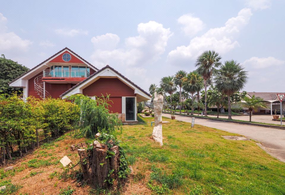 a red wooden house surrounded by grass and trees , with a dirt road leading up to it at OYO 926 Sydney Resort