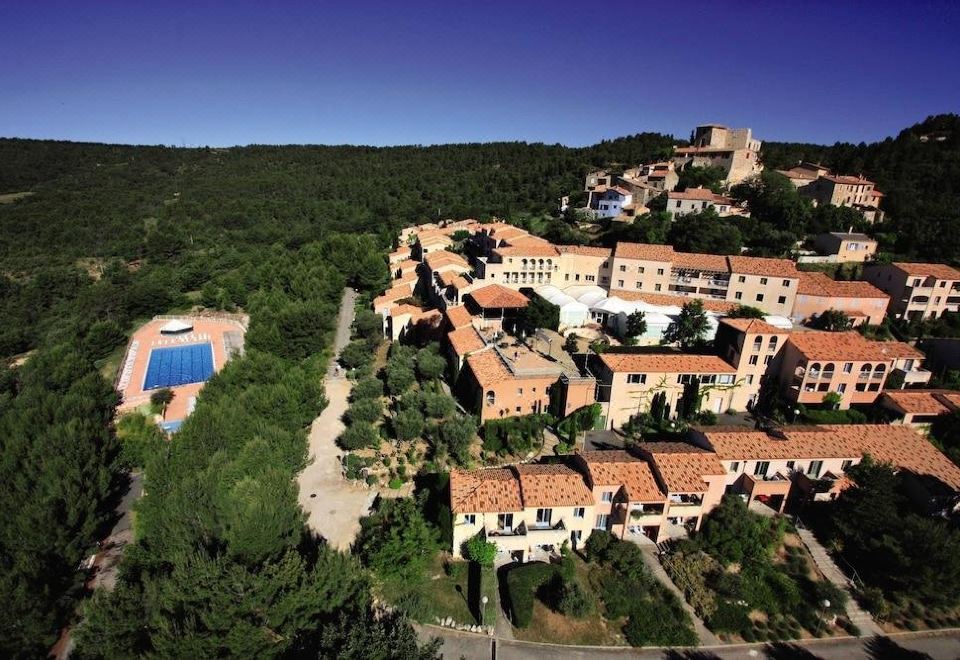 a large , red - roofed building with orange roofs situated on a hillside , surrounded by trees and hills at Belambra Clubs Montpezat - le Verdon