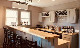 a bar area with wooden counter and chairs , white cabinets , and wine bottles on display at Plum Point Lodge