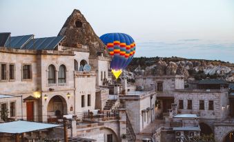 a hot air balloon is soaring high in the sky above a stone building , surrounded by other hot air balloons and buildings at Sultan Cave Suites