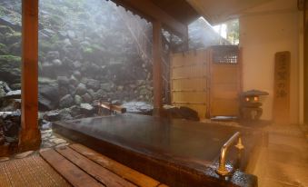 a traditional japanese bathhouse with wooden benches , a large bathtub filled with water and steam , and a stone wall decorated with rock formations at Osakaya Ryokan