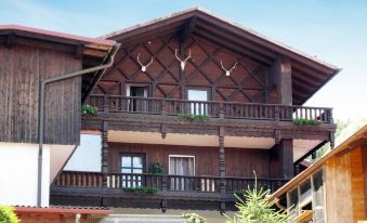 a wooden house with a balcony and antlers on the roof , surrounded by trees and grass at Drexler