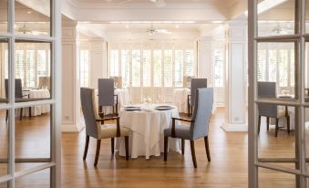 a white dining table with chairs is set in a room with wooden floors and large windows at The Atlantic Hotel