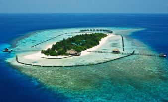 a tropical island with a few buildings and a walkway leading to it , surrounded by clear blue water at Komandoo Island Resort & Spa