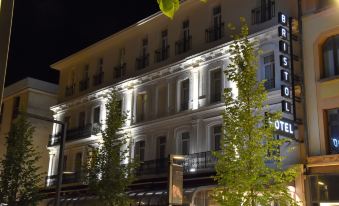 a large building with white and yellow lights on the balconies at night , illuminated by street lights at Hôtel le Bristol