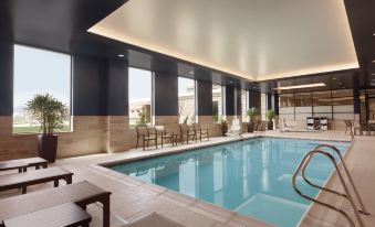 an indoor swimming pool with a large window , surrounded by lounge chairs and tables , in a modern hotel setting at Embassy Suites by Hilton South Jordan Salt Lake City