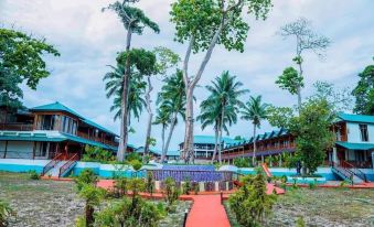 a tropical resort with palm trees , a red building , and a path leading to the entrance at Holiday Inn Beach Resort