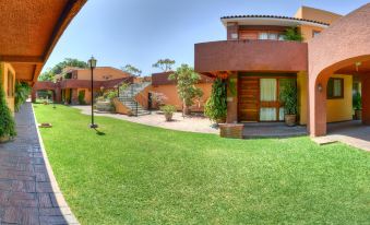 a man standing in front of a house on a grassy field , surrounded by trees at Hotel Hacienda