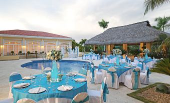 a large outdoor dining area with multiple tables set for a wedding reception , surrounded by a pool and tropical plants at Quality Hotel Real Aeropuerto Santo Domingo
