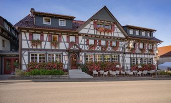 a large , old - fashioned building with a red and white tiled roof , surrounded by trees and flowers at Hotel Restaurant der Engel, Sasbachwalden