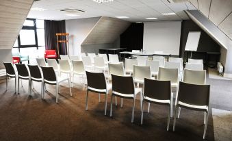 a conference room with rows of chairs arranged in a semicircle , and a projector screen on the wall at Logis Golfe Hotel