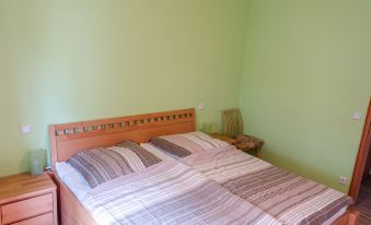 a well - lit bedroom with green walls , wooden bed frame , and striped bedding , as well as a nightstand and a small table at Raeck