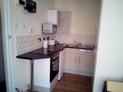 a small kitchen with white walls and a black countertop , equipped with a sink , stove , microwave , and dishwasher at Moon Face