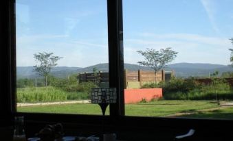 a window with a view of a grassy field and mountains , with a red wall in the foreground at Punto y Aparte
