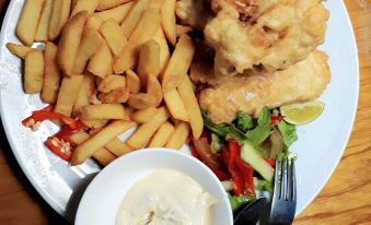 a white plate with fish and french fries , accompanied by a side of vegetables and a small bowl of dip at Suva Motor Inn