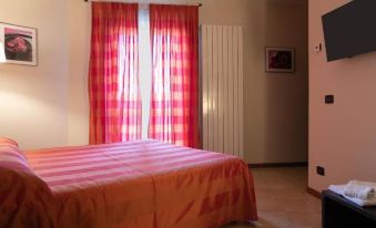 a bedroom with a red and pink plaid bedspread , a red window curtain , and a white radiator at Hotel Del Corso