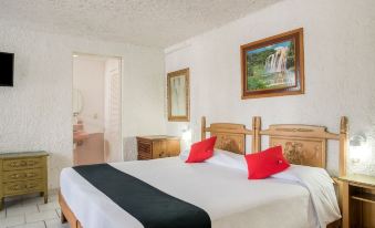 A bedroom with two beds, adorned with red pillows, is located next to an open door at Capital O Farallon Inn