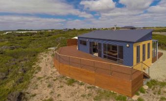a house with a blue roof and yellow walls is surrounded by a wooden deck in the middle of a grassy area at Seaspray