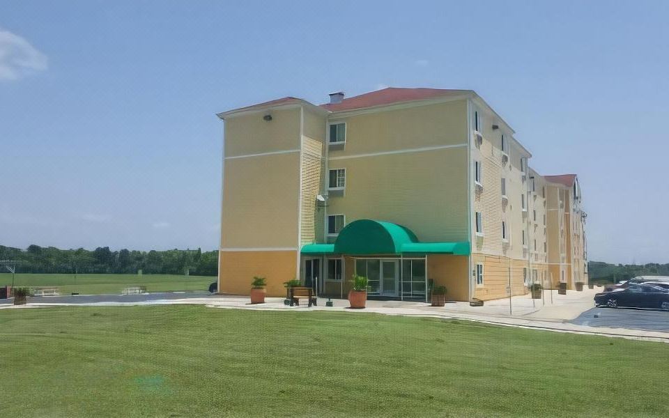 a large yellow and green building with a green awning is surrounded by a grassy area at Amelia Extended Stay & Hotel