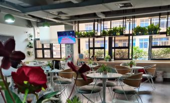 A restaurant in an urban setting with tables, chairs, and large windows overlooking the outside at Qiyou Capsule Youth Hostel