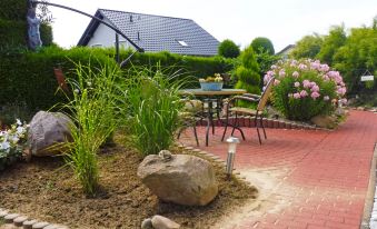 a brick patio surrounded by grass and plants , with a table and chairs placed near the edge of the space at Lona