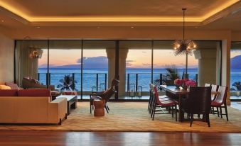 a modern living room with a large window overlooking the ocean , featuring a dining table , chairs , and couches at Four Seasons Resort Maui at Wailea