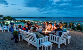 a group of people are sitting on white benches around a fire pit , enjoying each other 's company during a nighttime gathering at Oak Island Resort & Conference Centre