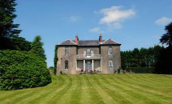 a large , two - story stone house with a red roof and chimneys , surrounded by a lush green lawn and trees at Boulston Manor