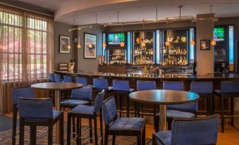 a modern bar with blue chairs , wooden tables , and a long counter filled with liquor bottles at Courtyard Newark-University of Delaware
