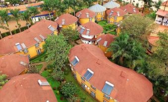 aerial view of a cluster of yellow houses with red roofs surrounded by trees and grass at Silver Springs Hotel Uganda