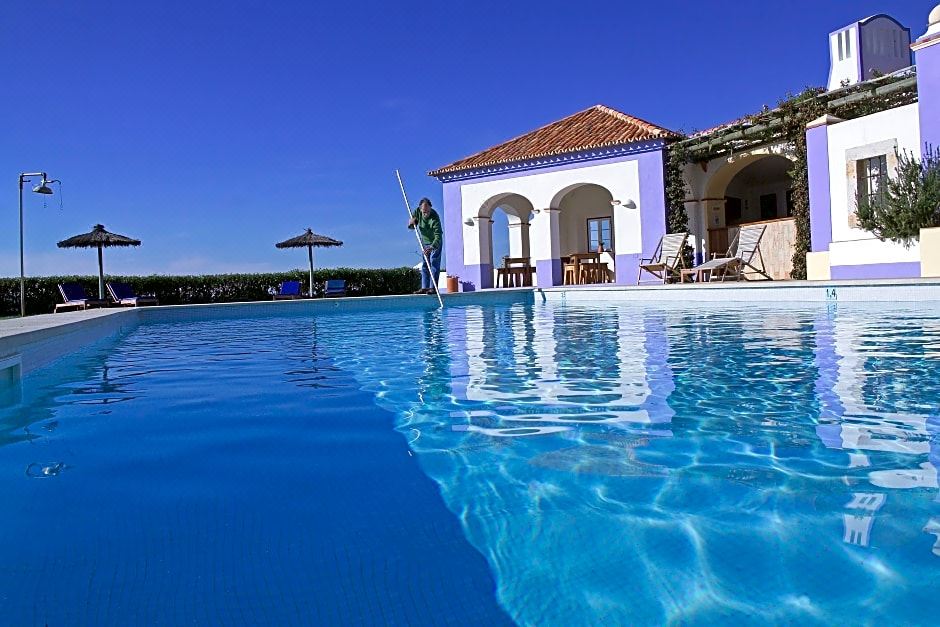 a large swimming pool with a house in the background and an umbrella on the side at Herdade Do Touril