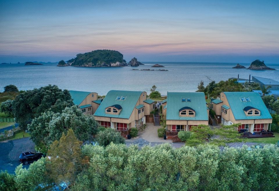 aerial view of a row of small , two - story houses on the coast , surrounded by trees and overlooking the ocean at Hahei Beach Resort