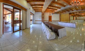 a large room with long tables and chairs , all covered in white tablecloths , under a wooden ceiling with exposed beams at Hotel Hacienda