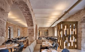 a restaurant with stone walls , wooden columns , and arches , containing tables , chairs , and a couch at The Setai Tel Aviv, a Member of the Leading Hotels of the World