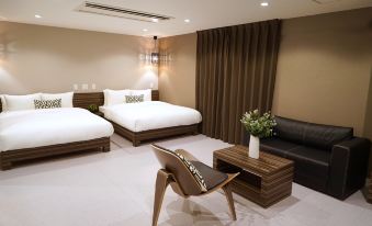 a modern bedroom with two beds , a chair , and a wooden table , all arranged in a minimalist style at Hotel 88 Shinsaibashi
