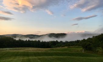 a serene landscape with a mountain range in the distance , green grass , and a foggy sky at Fat Sheep Farm & Cabins