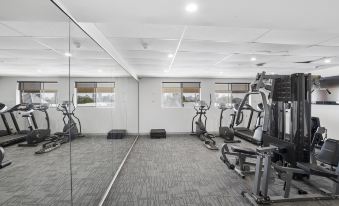 a gym with various exercise equipment , including treadmills and weight machines , is reflected in a large mirror at Metro Hotel Perth