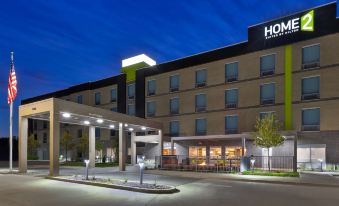 a modern hotel building with a large sign above the entrance , illuminated by lights at night at Home2 Suites by Hilton Battle Creek