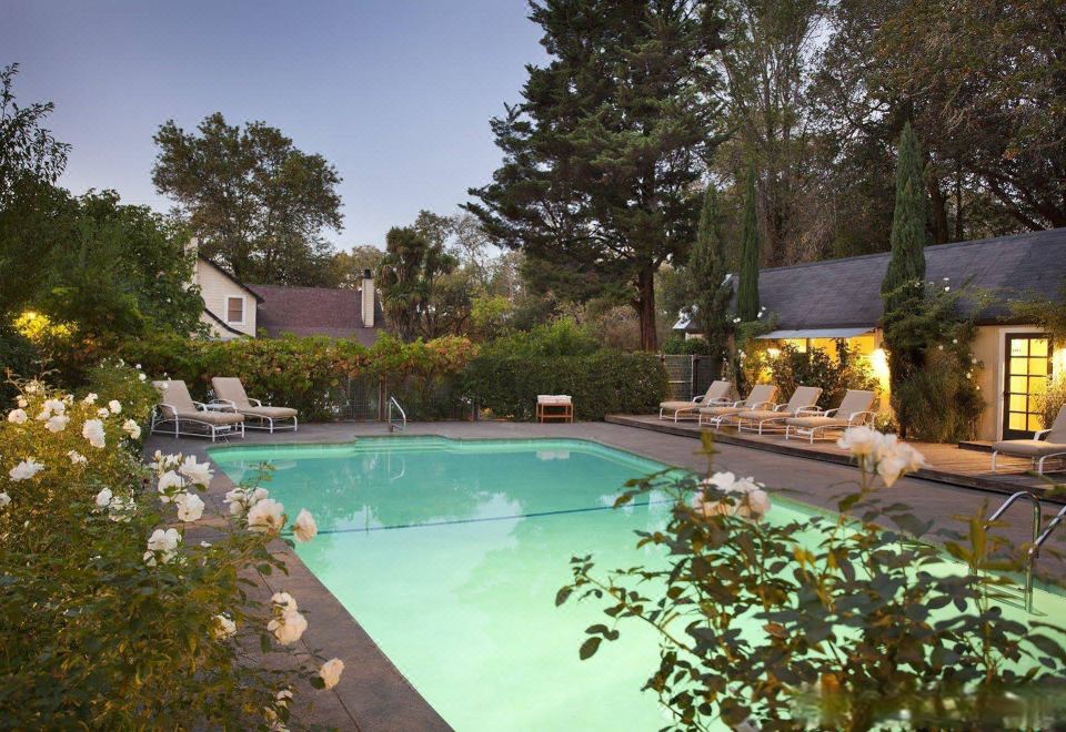 a large , well - maintained swimming pool surrounded by lush greenery and flowers , with several lounge chairs placed around it at Farmhouse Inn