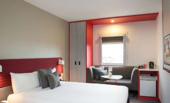 a modern hotel room with a large bed , white bedding , and red accents , along with a window and chair at Ibis Sydney Airport