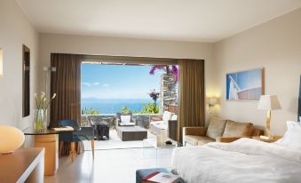 a bedroom with a bed , chairs , and a sliding glass door leading to a balcony overlooking the ocean at Daios Cove