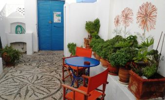 a patio with a blue table and chairs , surrounded by potted plants and a white door at Angelica