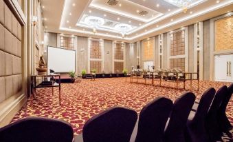 a large , empty conference room with red carpet and gold accents , equipped with rows of chairs and tables at Savero Hotel Depok