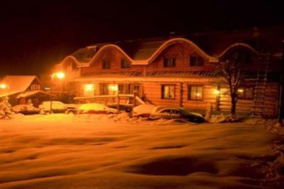 a snow - covered town at night , with several cars parked in front of a large wooden house at Troll