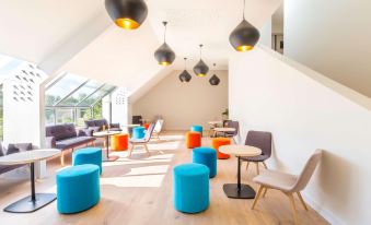 a modern living room with a variety of seating options , including blue and orange ottomans , wooden floors , and pendant lights at Best Western Armor Park Dinan